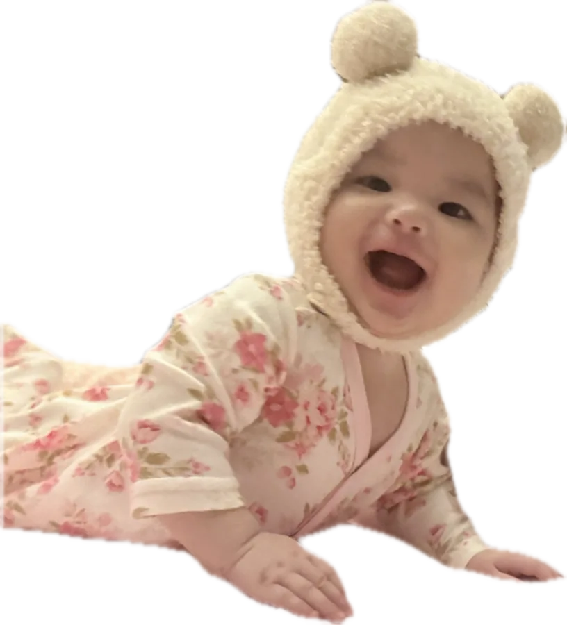 Aria laughing, crawling forward in a floral sleepsuit and bear-ear hat